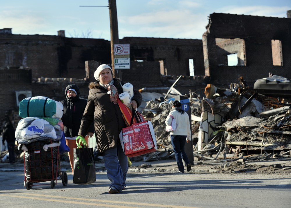 After getting household supplies from a nearby distribution center, people walk home past burned out businesses in the Rockaway Park section of Queens November 14, 2012 in New York as the city recovers from the effects of super storm Sandy. (AFP PHOTO...