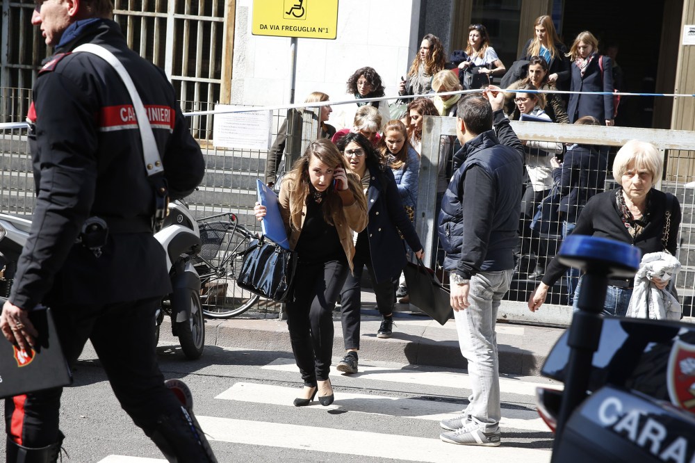 A plainclothes policeman helps to evacuate people from the tribunal building in Milan, Italy, after a shooting was reported inside a courtroom on April 9, 2015. (Photo by Luca Bruno/AP)