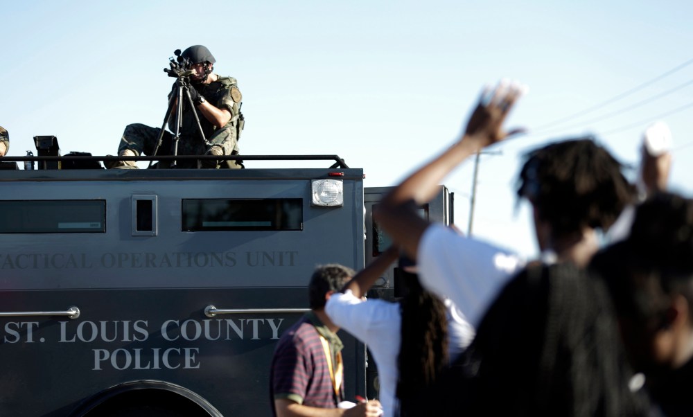 A member of the St. Louis County Police Department points his weapon in the direction of a group of protesters in Ferguson, Mo. on Wednesday, Aug. 13, 2014.