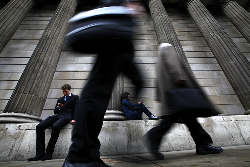 A man and woman use their mobile phones as commuters walk past the columns of the Bank of England in the City of London, July 3, 2012.  (Photo by Andrew Winning/Reuters)