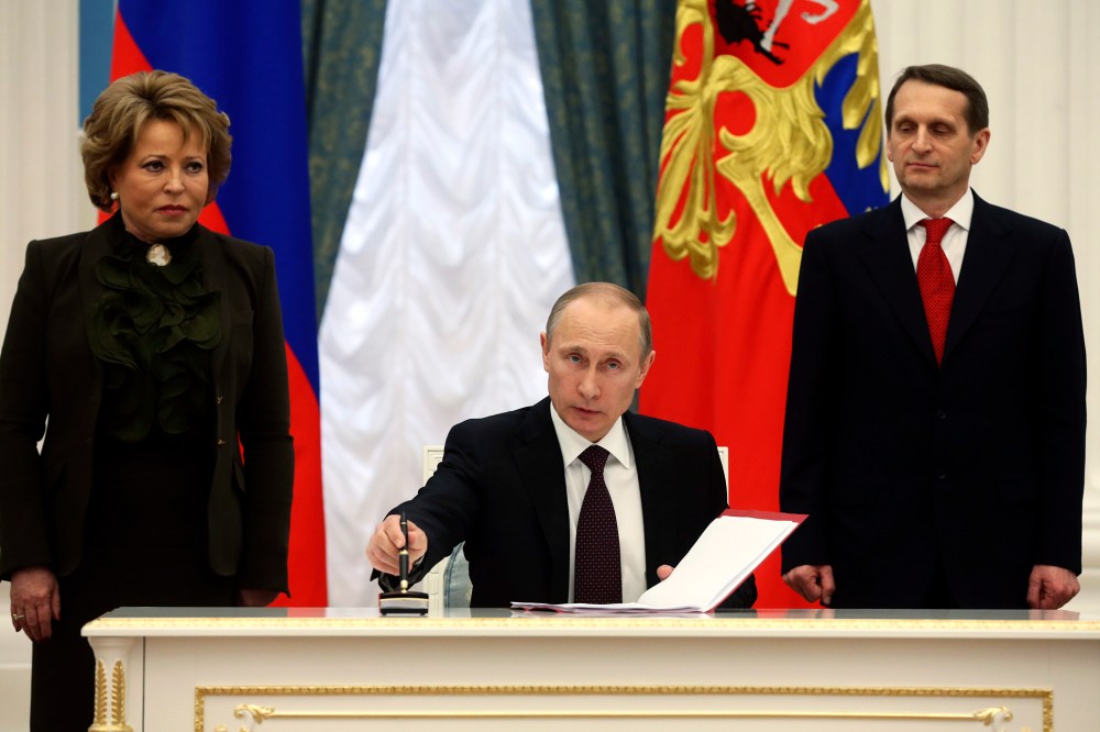 Russian President Vladimir Putin (C) prepares to sign documents as Sergei Naryshkin (R), speaker of the State Duma, Russia's lower parliament house, and Valentina Matviyenko, head of the Federation Council, look on during a ceremony in Moscow's Kremlin Ma