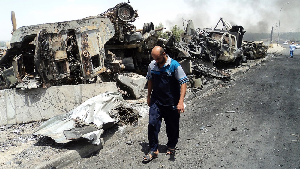 A man walks past near remains of burnt vehicles belonging to Iraqi security forces in the northern Iraq city of Mosul, June 13, 2014.