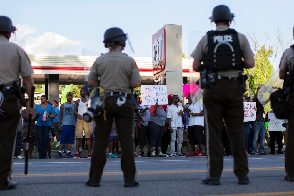 Police officers watch as demonstrators protest the death of black teenager Michael Brown in Ferguson, Mo. on Aug. 12, 2014 (Photo by Mario Anzuoni/Reuters)