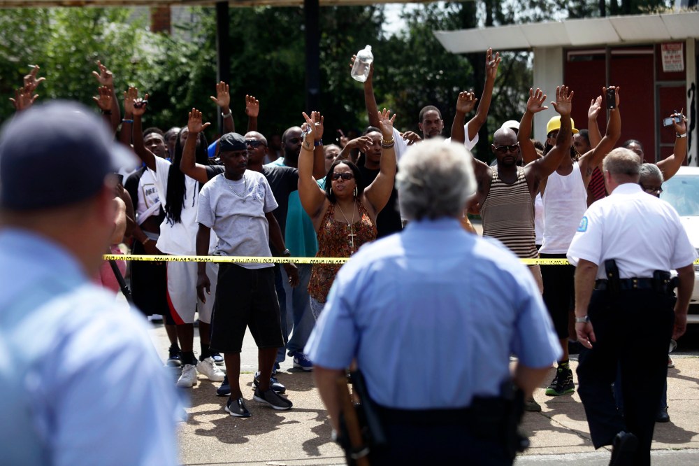 A crowd reacts to St. Louis Police Officers standing outside Golden Shears Barber & Beauty Shop where officers shot a man holding a knife in St. Louis, Mo., Aug. 19, 2014.