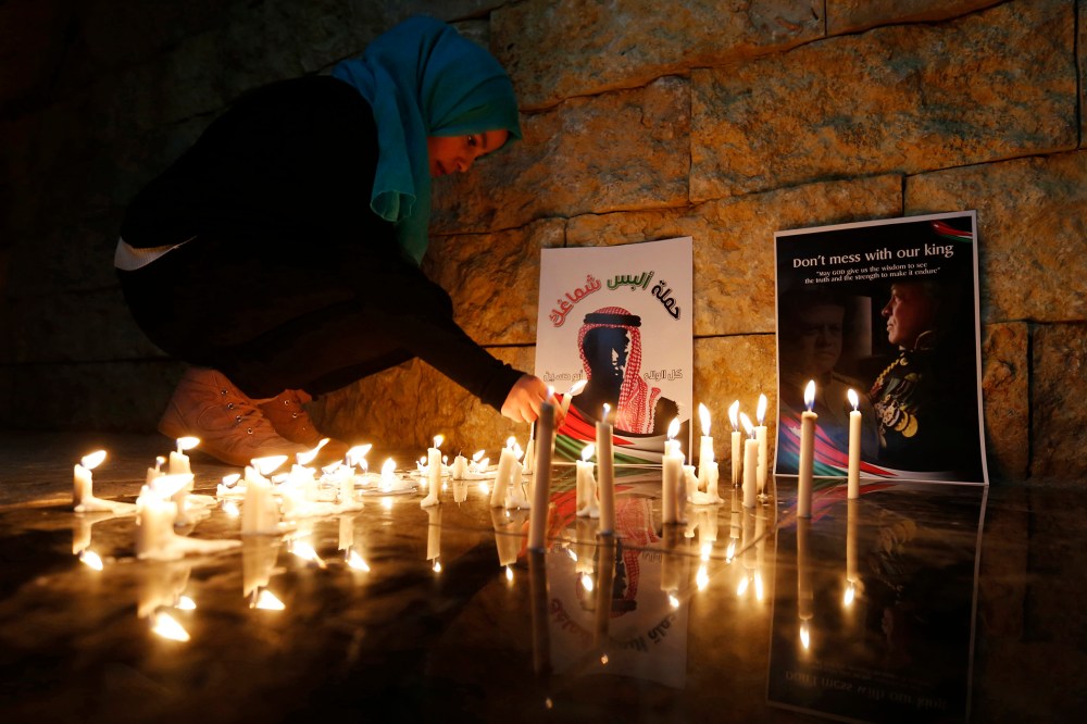 A Jordanian woman lights a candle near a poster of Jordan's King Abdullah (R) and a poster depicting Jordanian pilot Muath al-Kasasbeh during a candlelight vigil in Amman on Feb., 7, 2015. (Photo by Muhammad Hamed/Reuters)