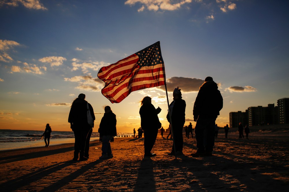 People stand with an American flag during a remembrance ceremony along the beachfront damaged by hurricane Sandy in October 2012 in the borough of Queens in New York