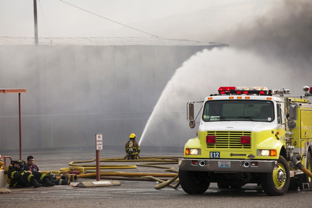 Firefighters rest as their colleague continues to battle flames that burned through the night at a commercial building that was ignited by the Sleepy Hollow fire in Wenatchee, Washington June 29, 2015. (Photo by David Ryder/Reuters)