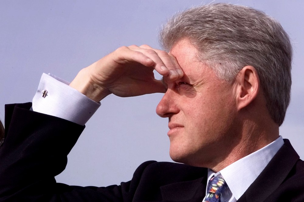 U.S. President Bill Clinton shades his eyes as he waits to be introduced at an event in Newport, R.I. in 1998.