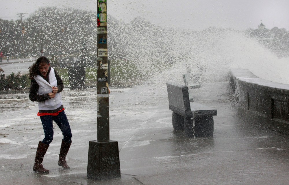 A woman reacts to waves crashing over a seawall in Narragansett, R.I., Monday, Oct. 29, 2012. Hurricane Sandy continued on its path Monday, as the storm forced the shutdown of mass transit, schools and financial markets, sending coastal residents...