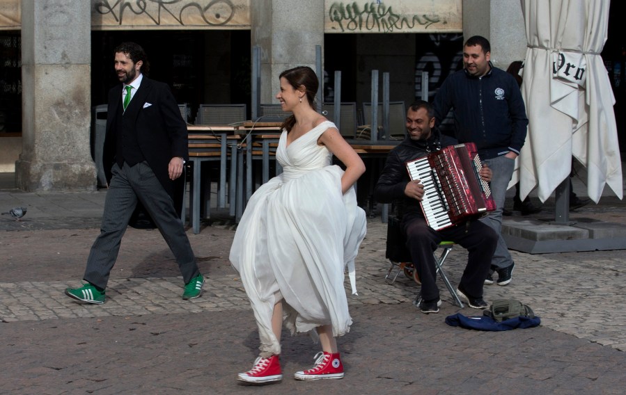A bride and groom walk past a street musician in Plaza Mayor, Madrid, Spain, Monday, Jan. 20, 2014.