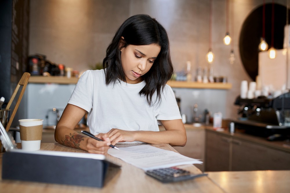 Female cafe owner signing papers calculating business expenses