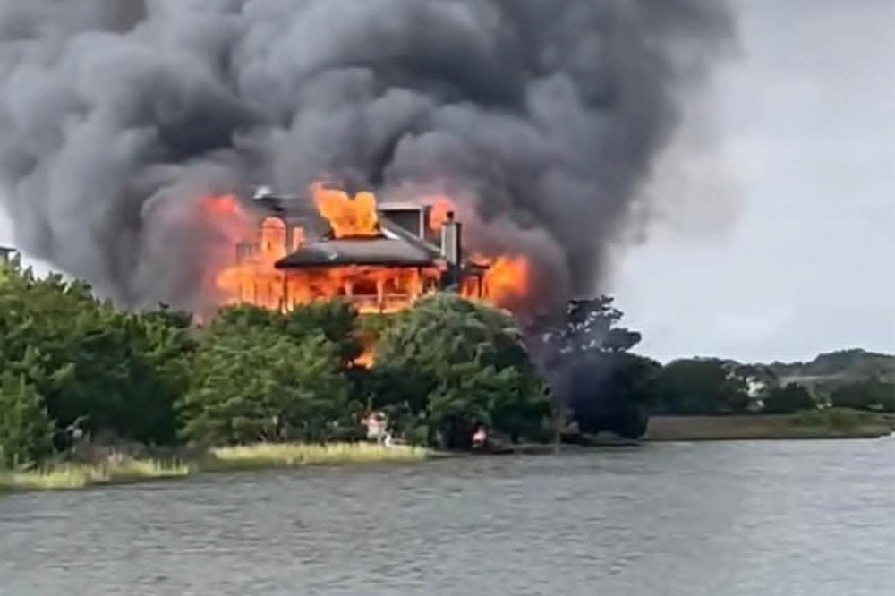A view of a home on fire near a body of water.