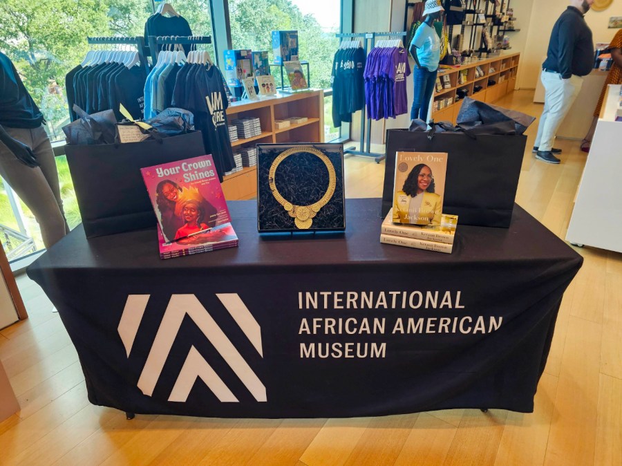 A table with books, gift bags, and a necklace on display in the center inside of a gift shop