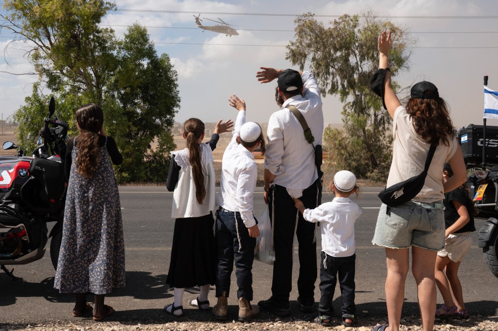 People with their backs to the camera wave at a helicopter.