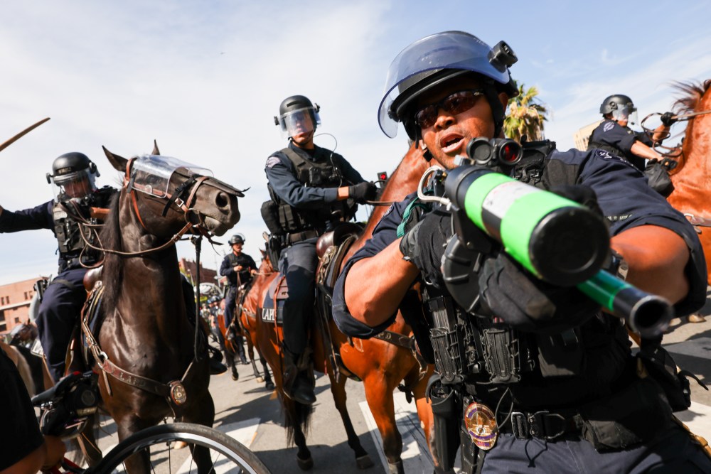 A police officer holds a weapon to the camera as protesters face off with police outside of a federal building in downtown Los Angeles for an anti-Trump "No Kings Day" demonstration.