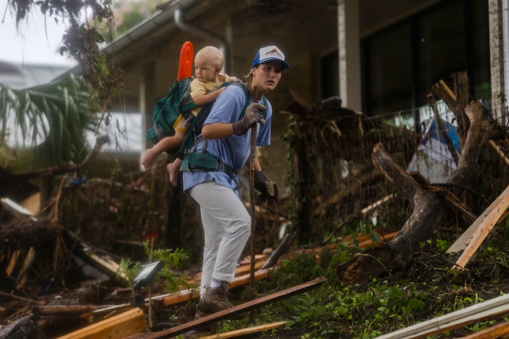 A search and rescue worker with a baby on their back looks through debris for any survivors or remains of people swept up in the flash flooding in Texas.