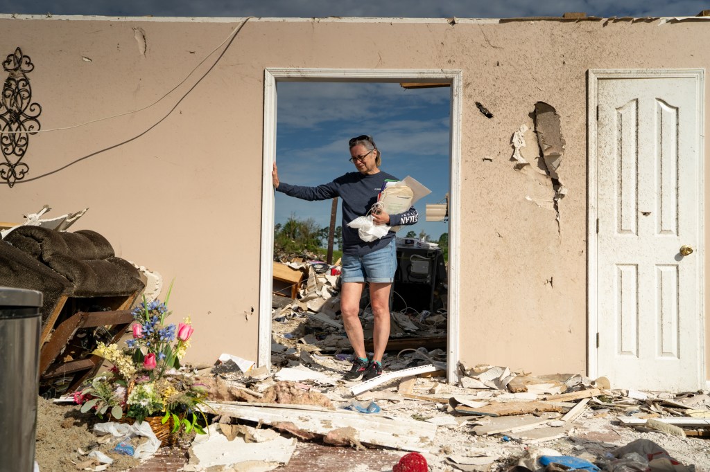 A woman stands in a doorway of a roofless home filled with debris after a tornado struck.