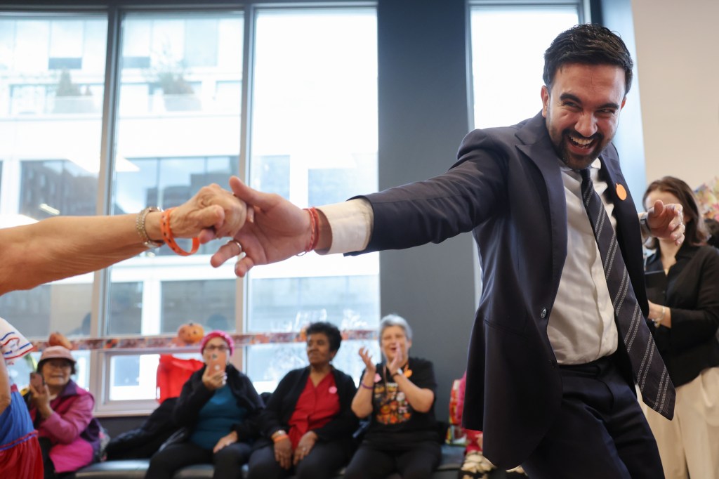 Zohran Mamdani reaches out as a person out of frame grabs his hand.