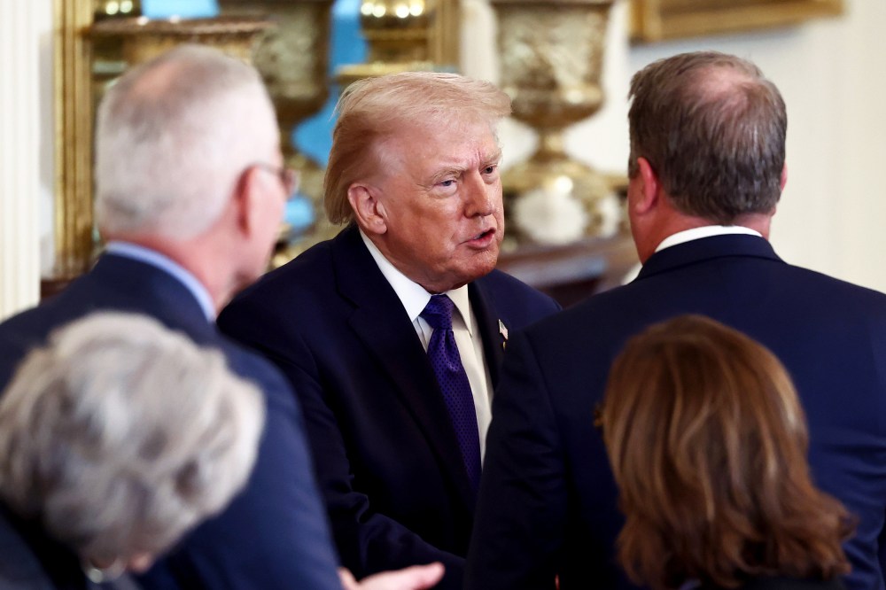 President Donald Trump speaks with people who have their back turned toward the camera.