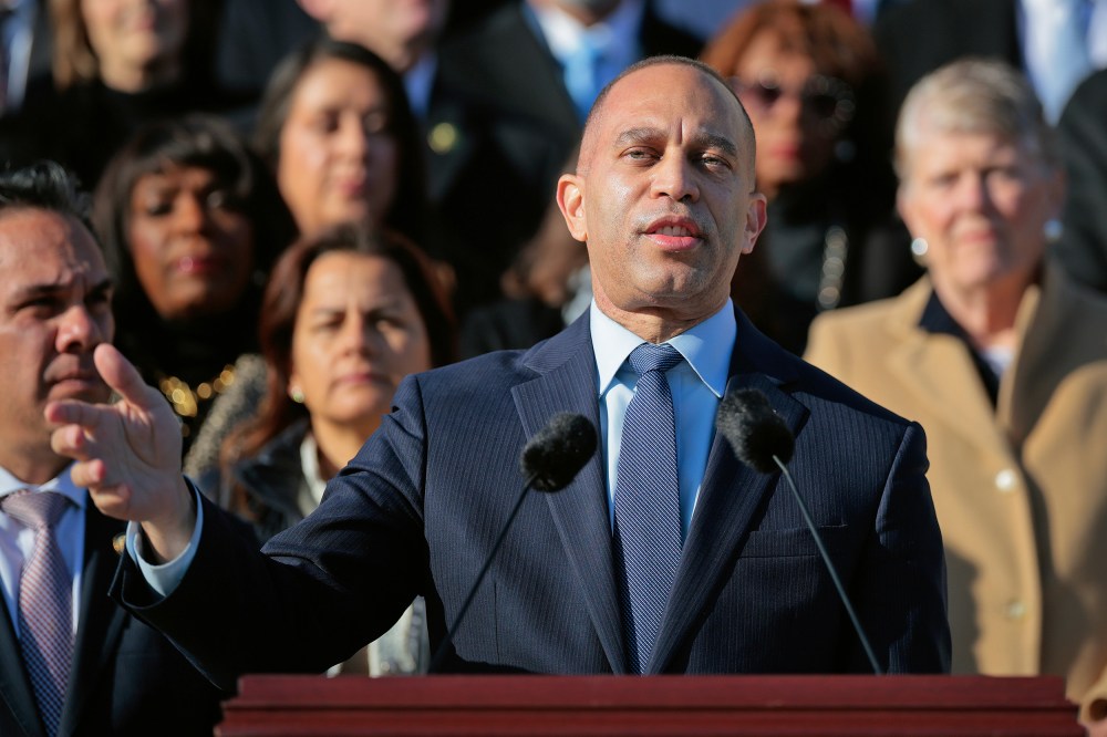 Hakeem Jeffries stands at a podium in front of a crowd of other Democratic leaders.