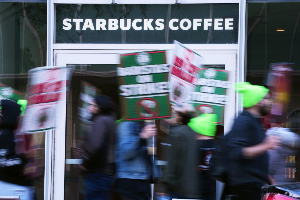 People blurred in motion hold signs in front of a Starbucks Coffee location.