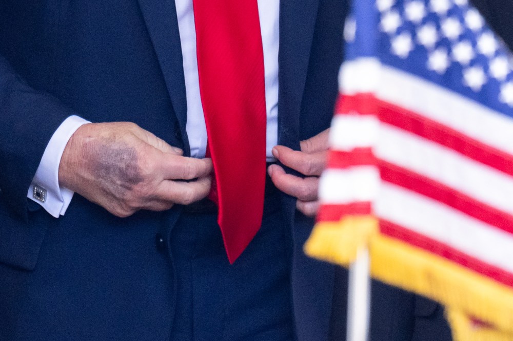 A close-up of Donald Trump’s right hand is seen as he buttons his jacket behind an American flag.