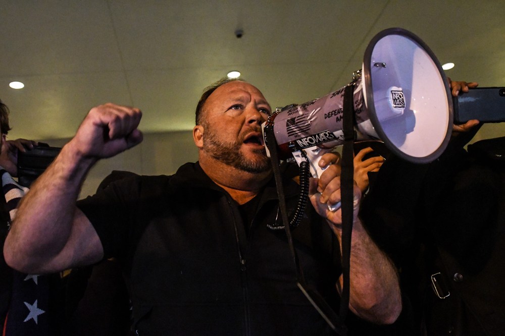 Alex Jones has one fist raised and holds a megaphone with the other hand.
