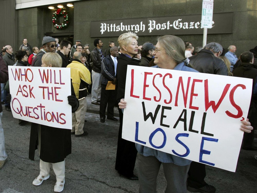 People hold signs reading "Who will ask the questions" and "Less news we all lose" outside the Pittsburgh Post-Gazette building.