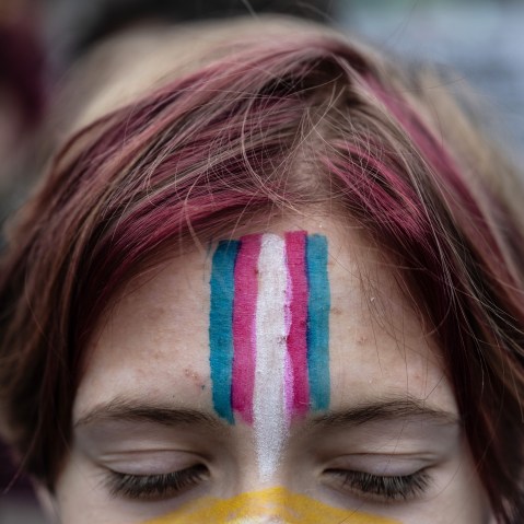 A demonstrator, as seen from the eyes up, looks down. They have a face painting of the trans flag on their forehead.