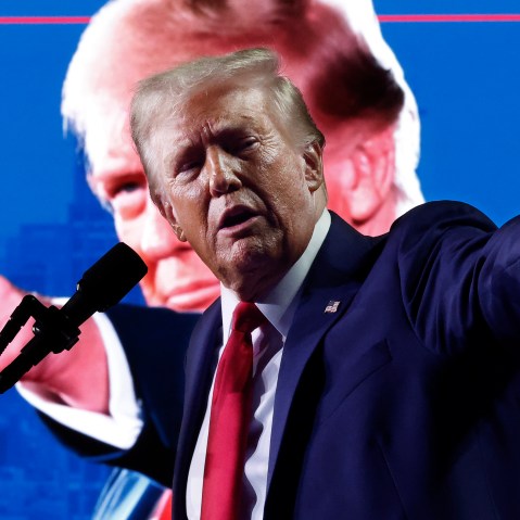 Donald Trump points at the crowd from the stage. His photo doing the same thing can be seen in the background.