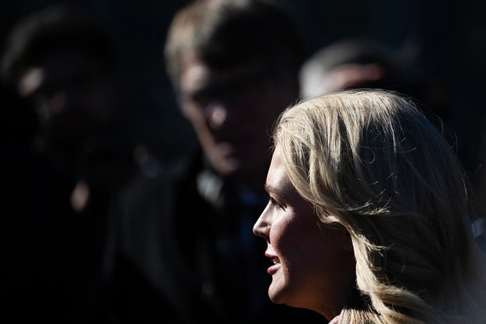 Press secretary Leavitt talks outside the White House, in a frame showing a very tight profile with members of the press in the background.