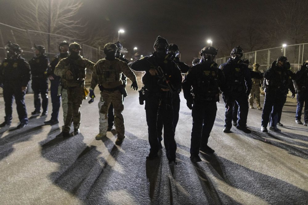 A line of ICE agents with guns drawn at nighttime.