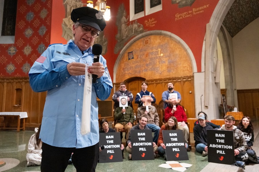 Randall Terry wears a police costume during a demo while he is opening a bag of long white zip ties to fake-arrest the participants.