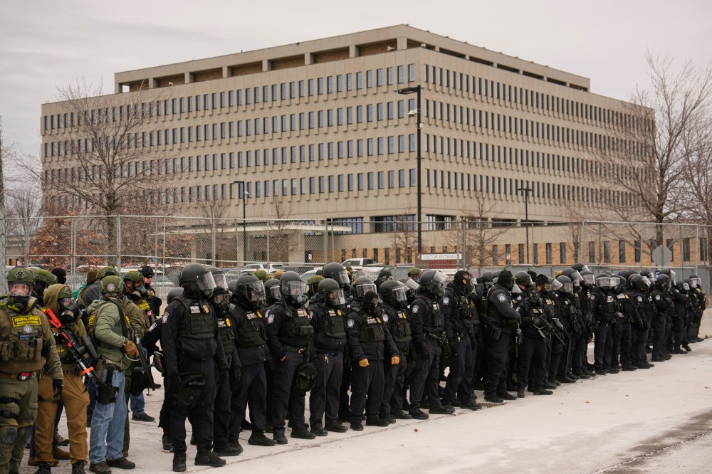 A crowd of federal immigration officers in helmets stand outside the Whipple Federal Building.