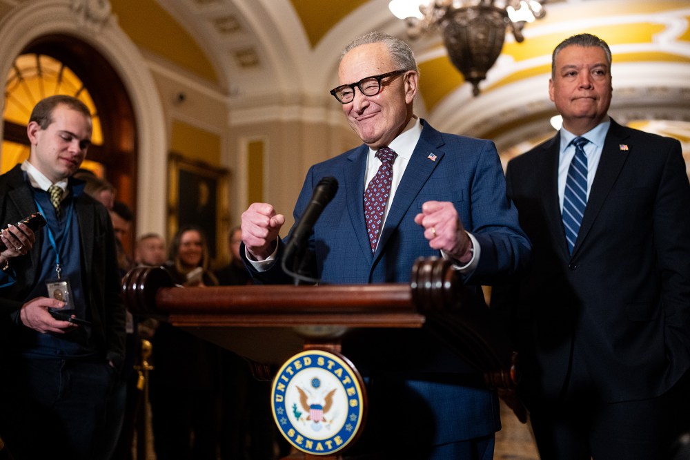Chuck Schumer pumps his fists in excitement behind a podium.