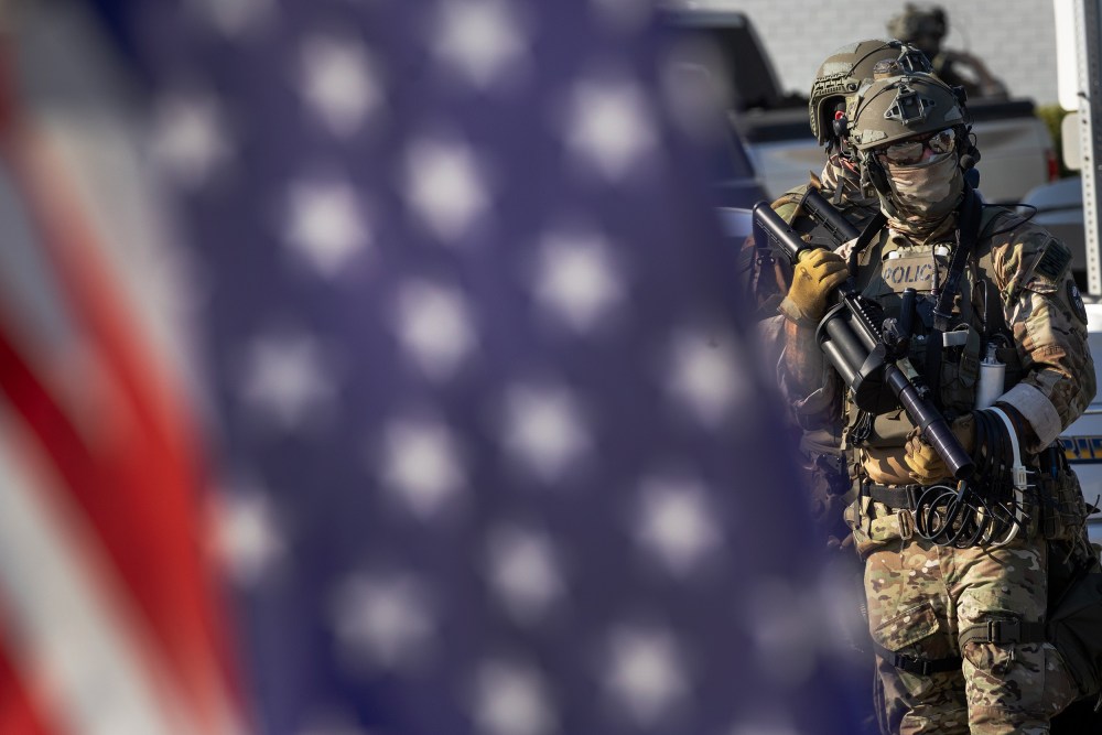 Federal law enforcement agents, right, with an American flag out of focus in the foreground.