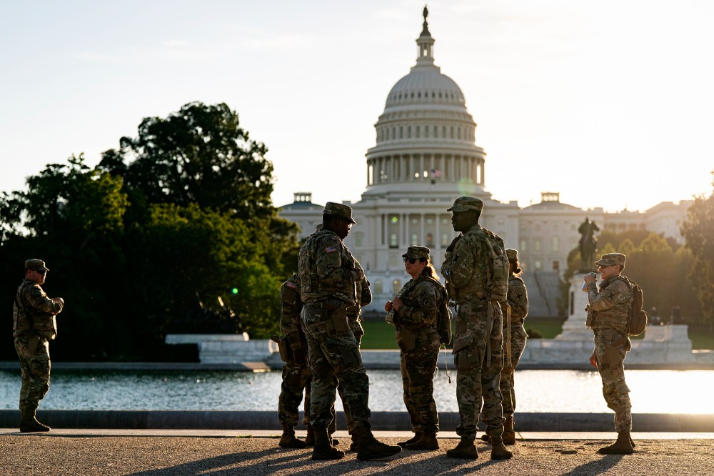 Several National Guard members stand by a pond across from the Capitol at sunset.