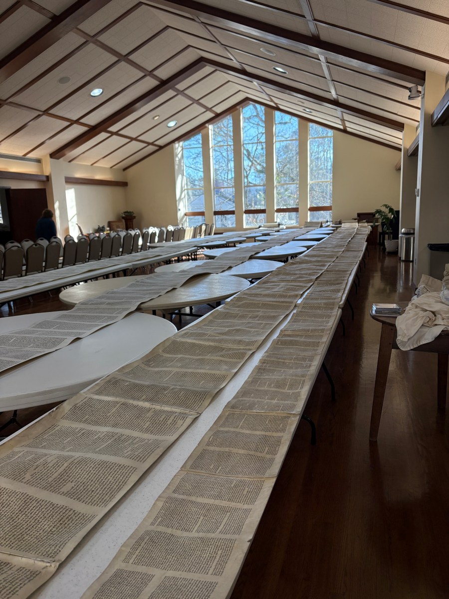 Unfurled Torah scrolls on foldable tables in a church.