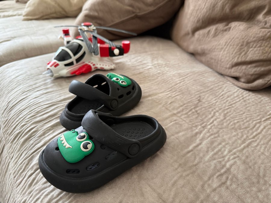 A pair of crocs shoes and a child's toy are seen on a couch