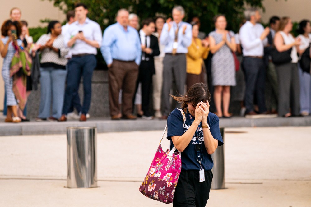 A person walks away with their head in their hands as people out of focus behind them clap and film.