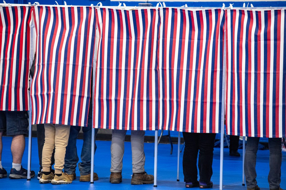 Legs are seen below red, white and blue voting booth curtains.