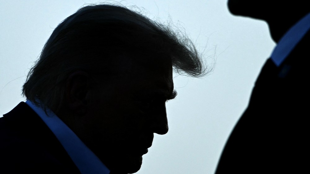 Trump's profile is seen as he walks up to the place. A security person stands on the right side.