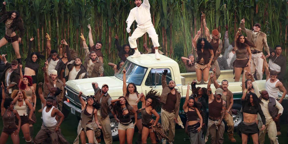Bad Bunny stands on the roof of a light yellow truck. People dance in the truck bed and on the football field below.