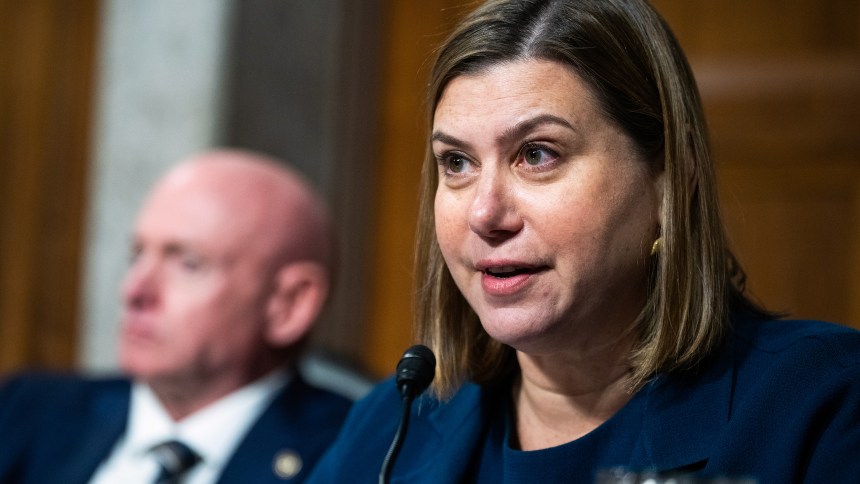 Elissa Slotkin, right, speaks into a microphone. Mark Kelly is out of focus behind her and to her left.