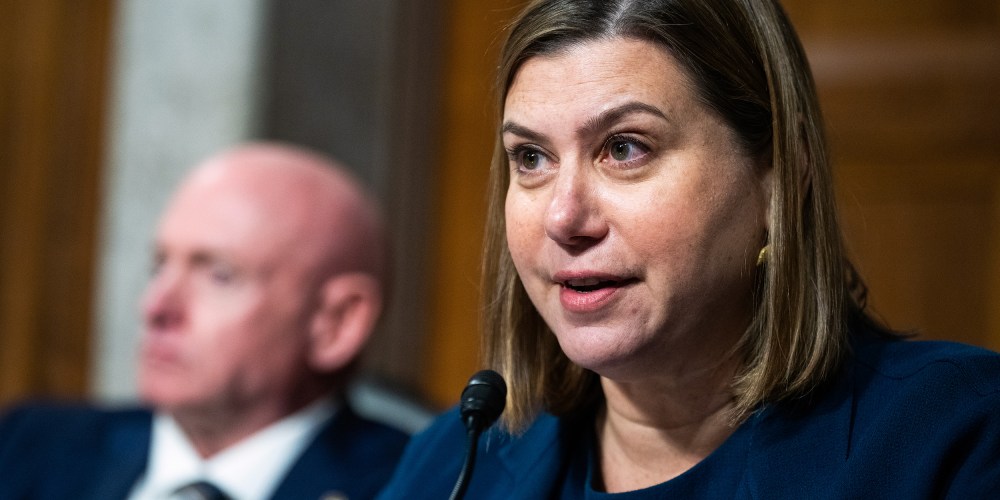 Elissa Slotkin, right, speaks into a microphone. Mark Kelly is out of focus behind her and to her left.