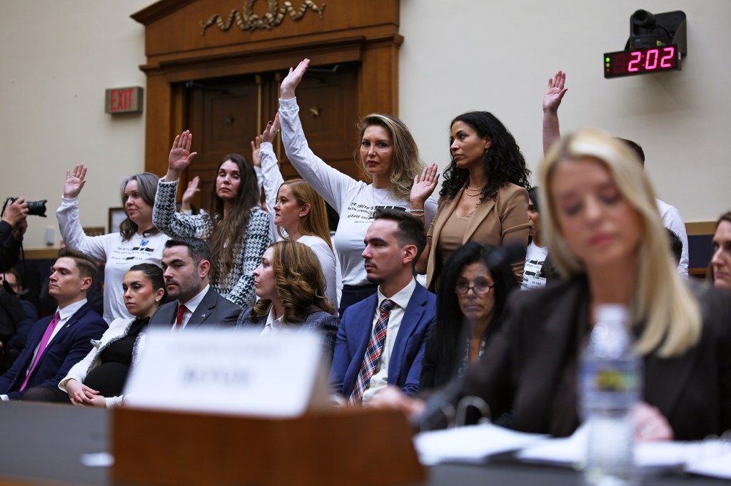 People raise their hands behind Pam Bondi, who is out of focus in the foreground.
