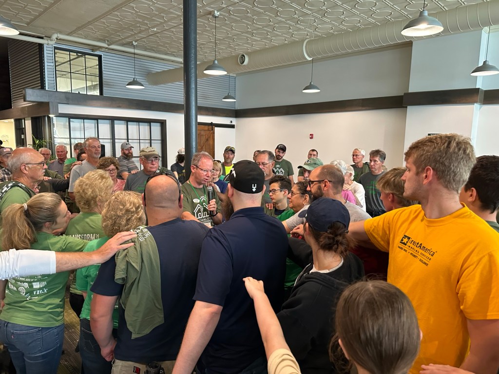 A group of people huddling around Clint Twedt-Ball reach their arms out toward him.