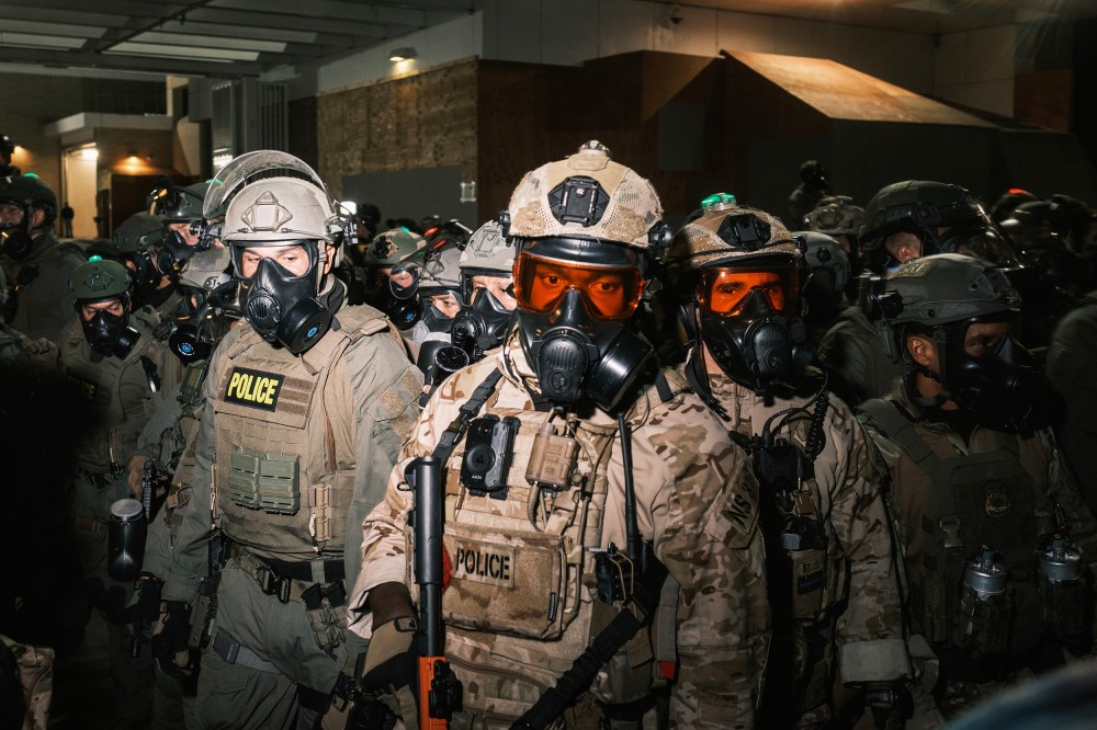 A crowd of federal officers in gas masks and helmets.
