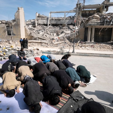 Men put their faces on the ground as they pray outside the ruins of a building.