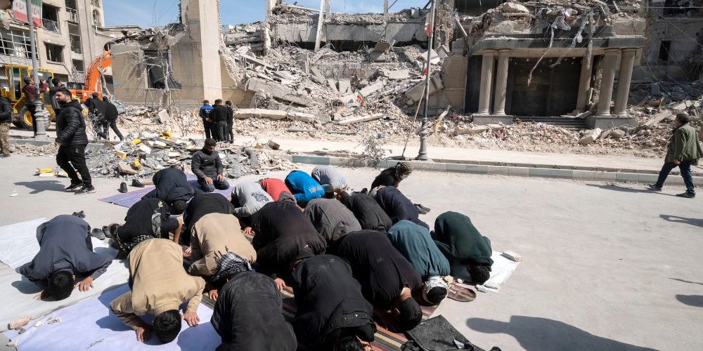 Men put their faces on the ground as they pray outside the ruins of a building.